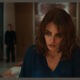Penélope Cruz, playing Sofia in the film Bunker, looks downward with a troubled expression in a blue v-neck top, while a blurry Javier Bardem, as Miguel, stands in the background.