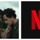 Two men with dark hair standing close outdoors under an overcast sky, with their foreheads touching; the man on the left wears a blood-stained light shirt, and the Netflix red "N" logo appears on a black background to the right.