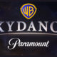 Combined logo graphic on a starry space background, featuring the yellow Warner Bros shield at the top, bold metallic text reading "SKYDANCE" in the center, and script text reading "Paramount" at the bottom.